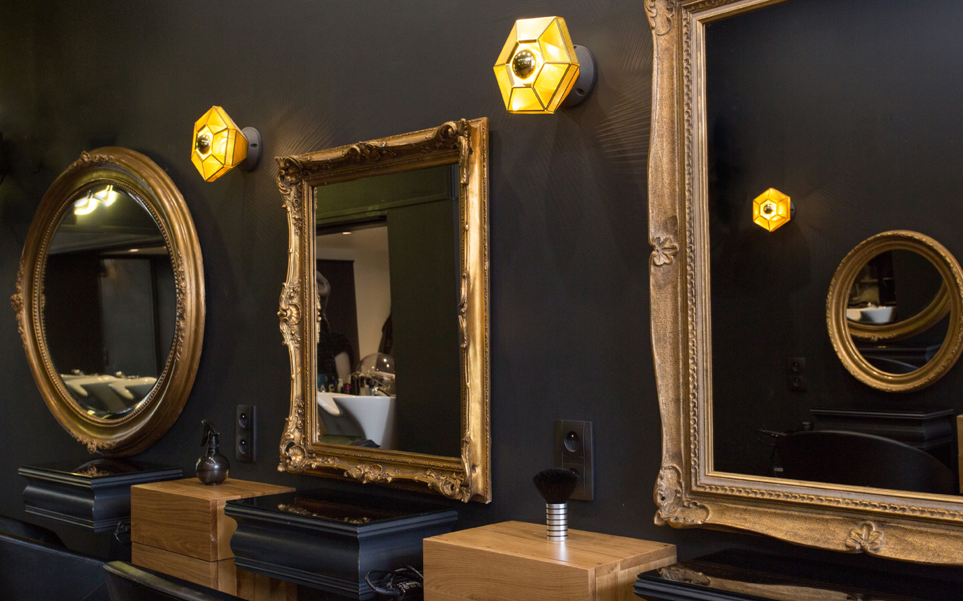 Espace coiffure avec des miroirs aux contours dorés et du mobilier noir.