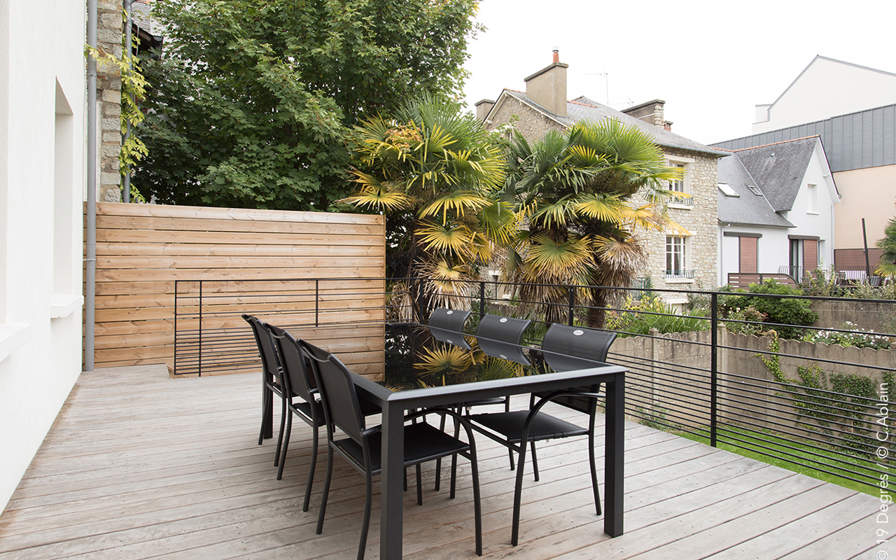 Terrasse en bois, garde du corps en métal et table à manger de jardin en métal et verre.