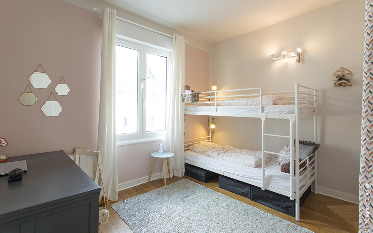 Chambre de fille avec un lit superposé blanc, des murs roses, un tapis gris et un plancher bois.