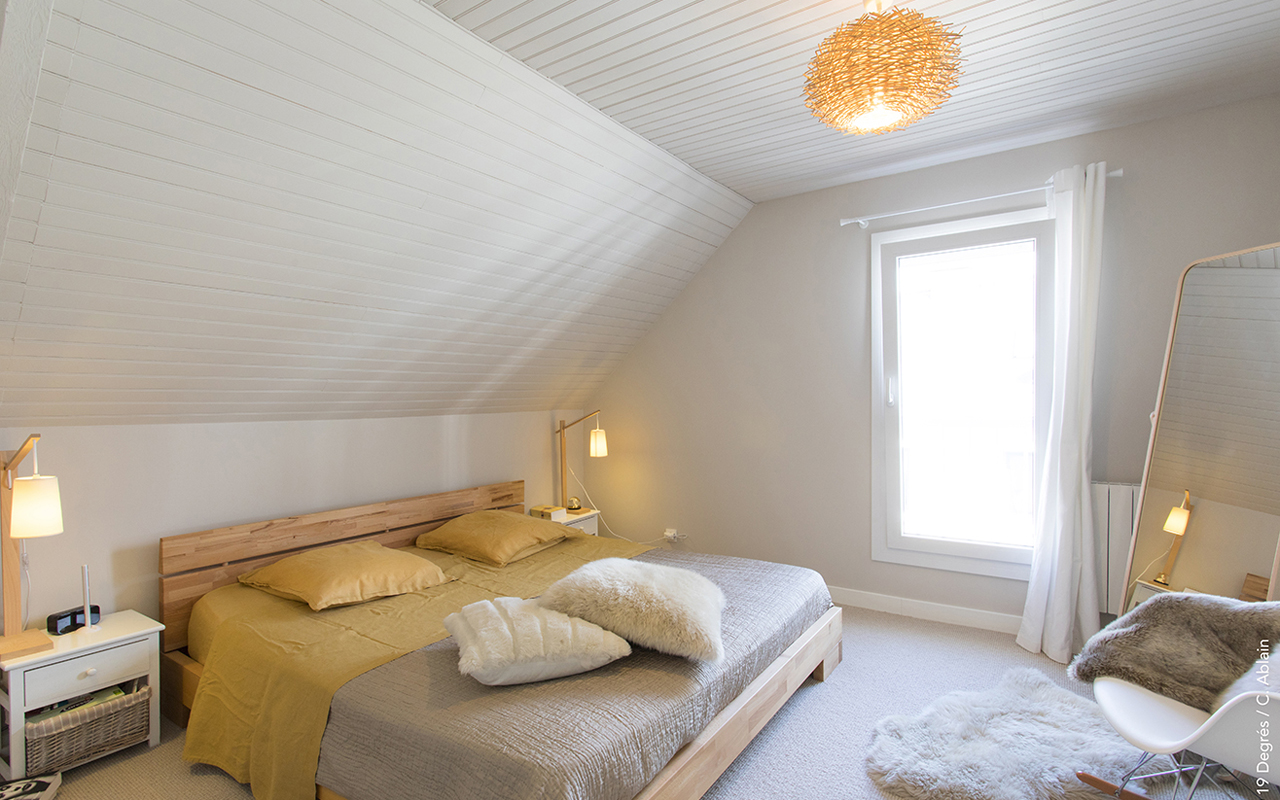 Chambre parentale avec un lit double, 2 tables de chevets et leur lampes de chevet. Une moquette au sol et un rocking chair scandinave.