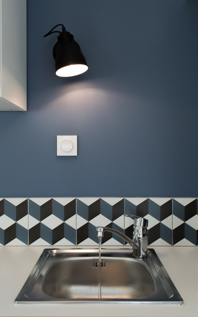 Evier de cuisine avec du carrelage à formes géométriques et un mur bleu.