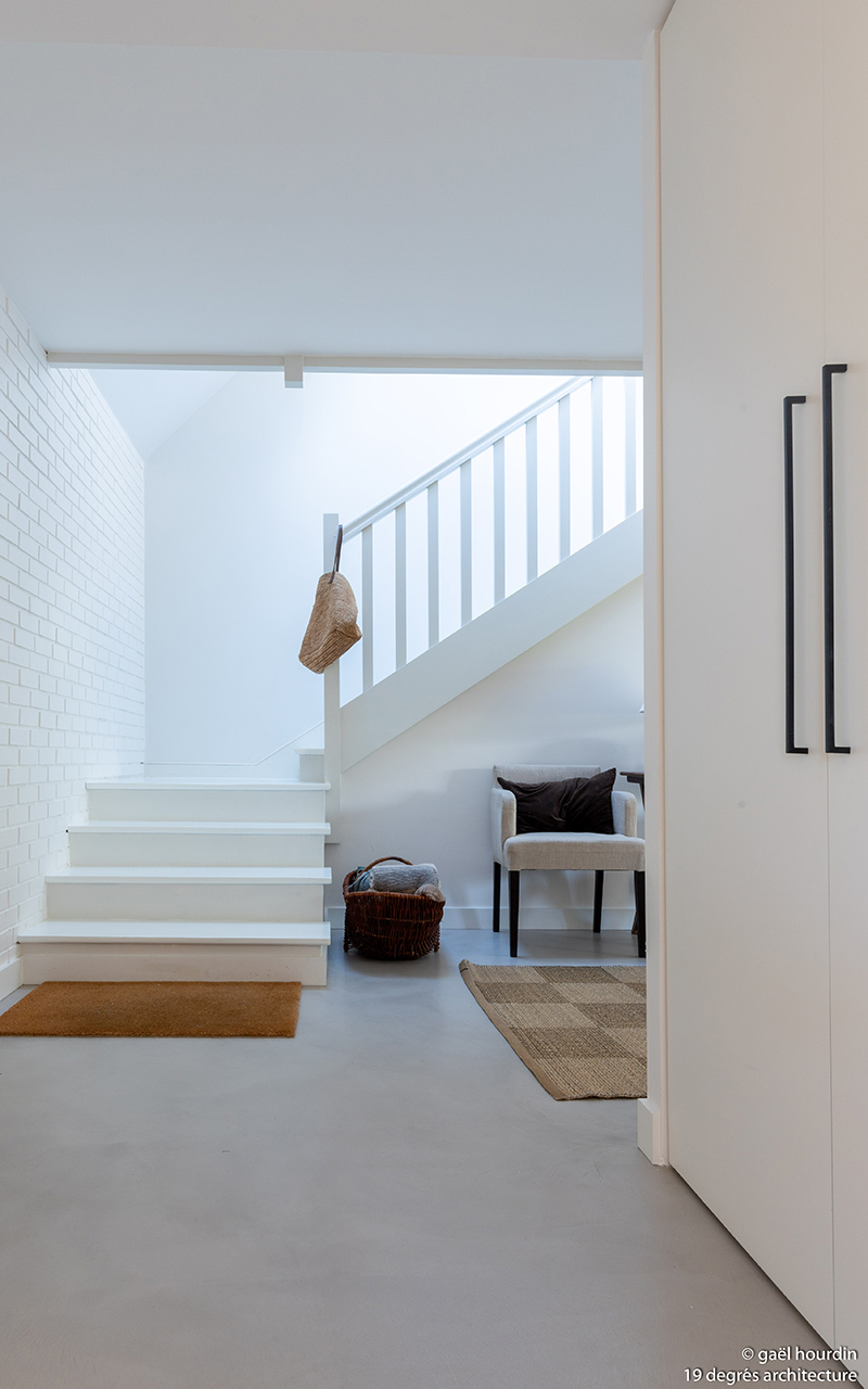 Couloir donnant sur un escalier blanc, un placard blanc et des fauteuils.