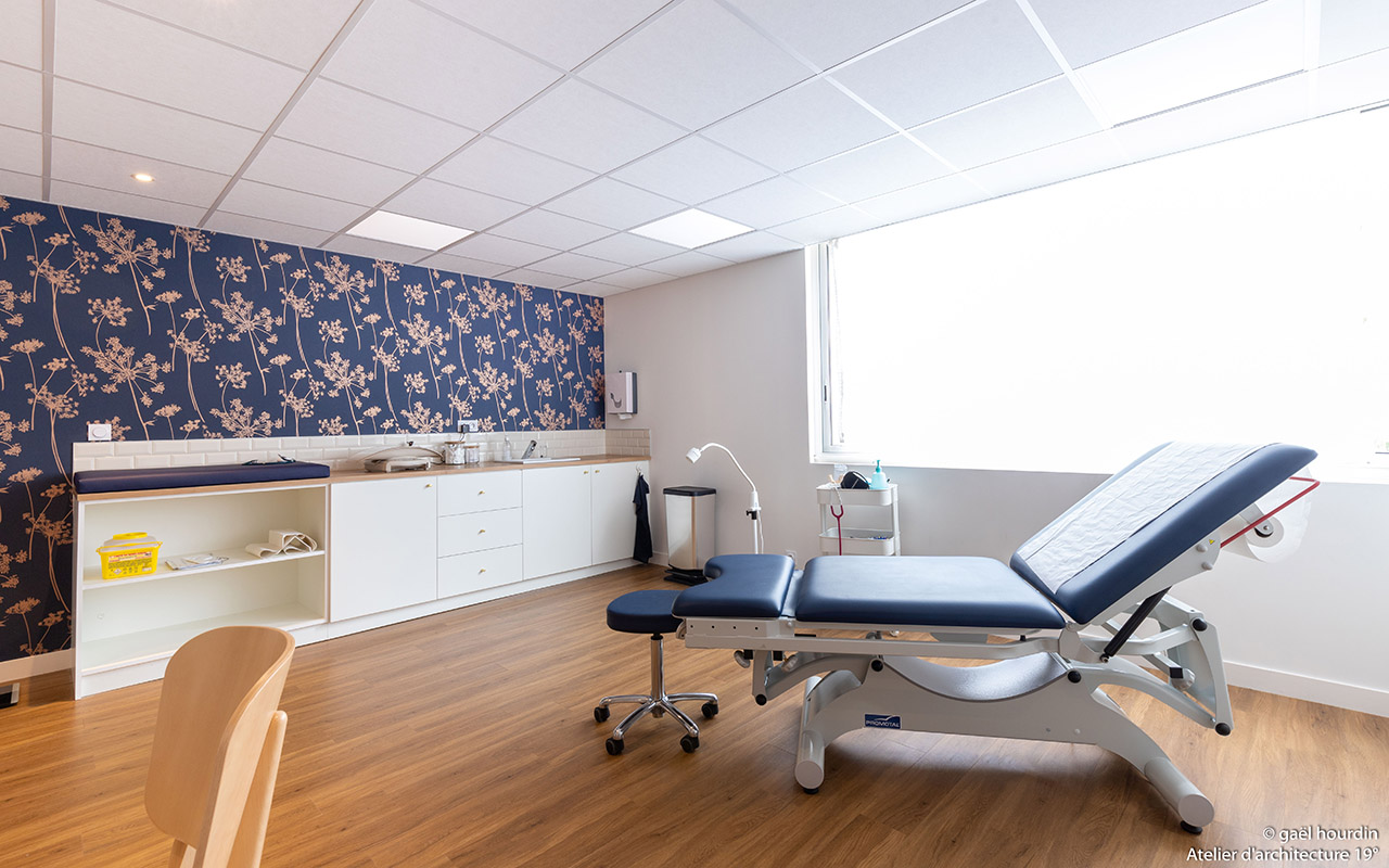 Salle de consultation avec un lit de consultation, un grand meuble de rangement et du matériel nécessaire pour un médecin.