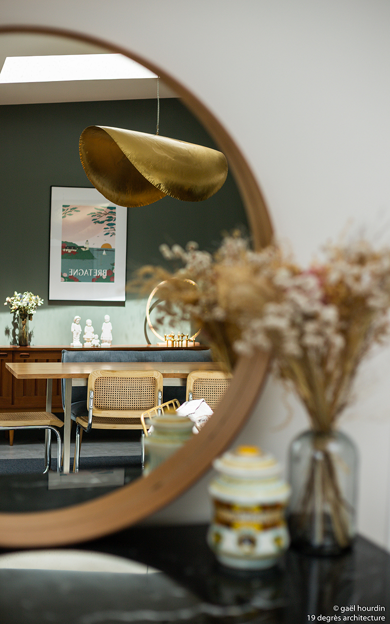 Vue sur la salle à manger à travers un miroir rond. La salle à manger possède un meuble avec de la décoration et une table avec des chaises.