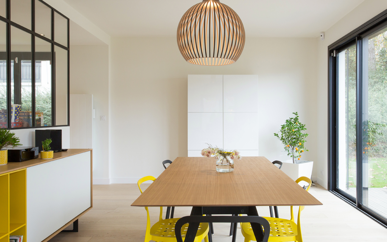 Salle à manger avec une table en bois et métal, des chaises en métal un meuble blanc et un meuble de salon en contre plaqué bois, blanc et jaune.
