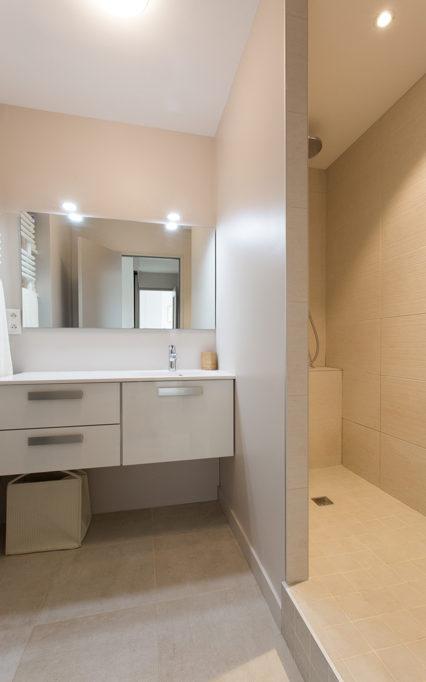 Salle de bain avec une douche carrelée, un vasque sur un meuble en hauteur ainsi qu'un miroir.