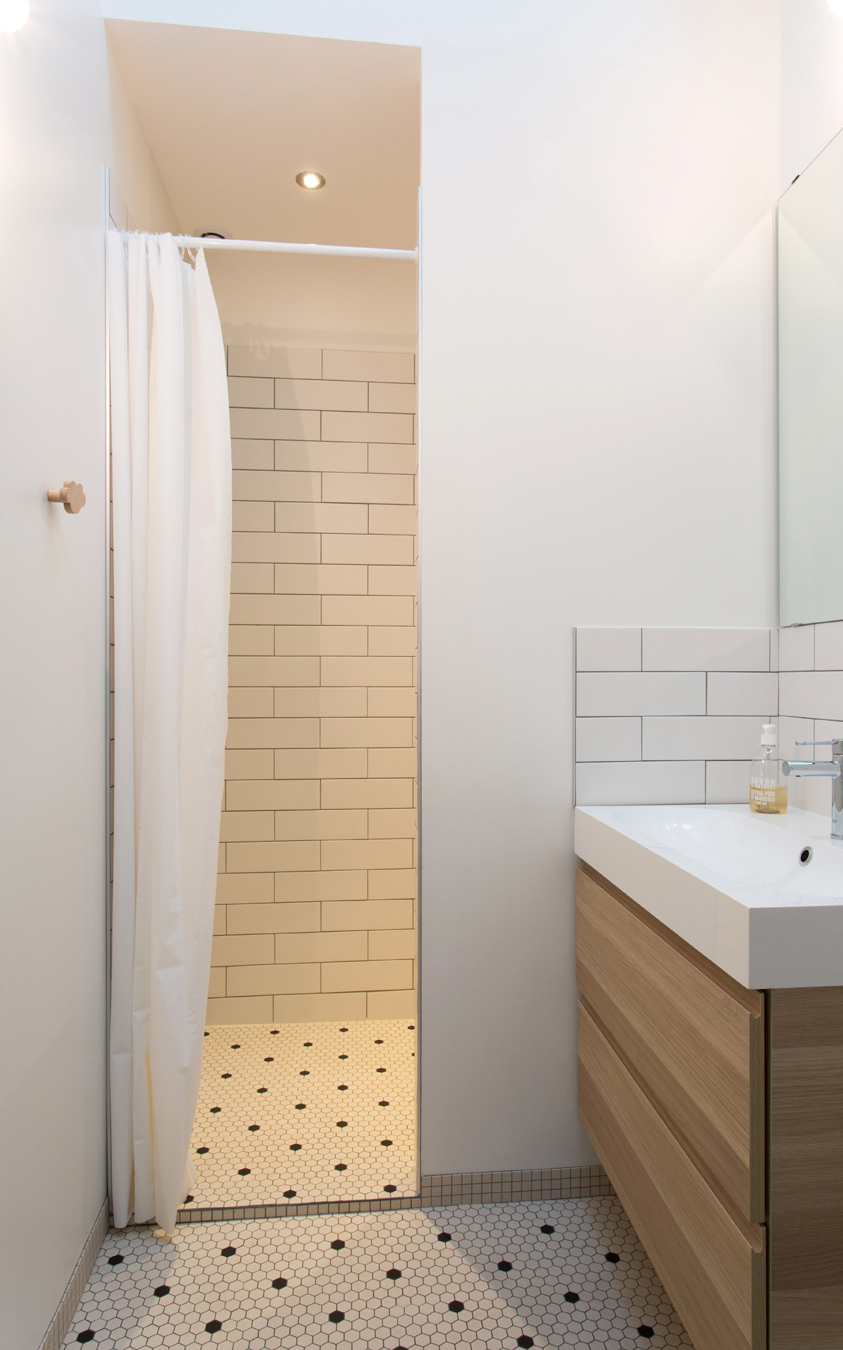 Salle de bain avec de la mosaïque blanche à poids noir, une douche et un vasque et son miroir.