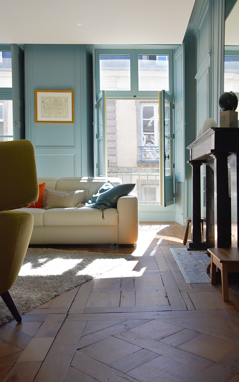 Salon avec des murs vert d'eau, une cheminée, un canapé blanc et un fauteuil jaune/vert.