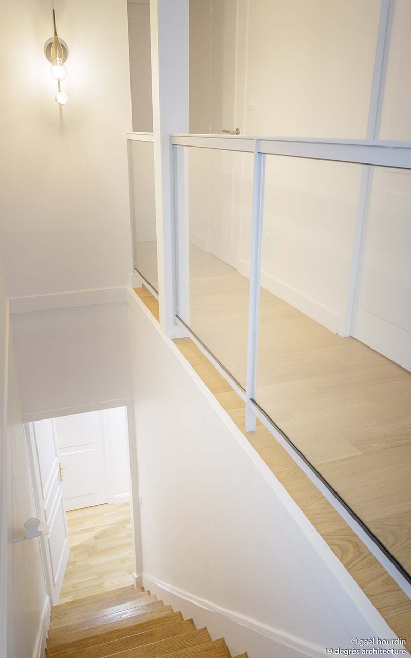 Haut de l'escalier. Les murs de l'étage et de l'escaliers sont blancs et les sols en parquet clair.