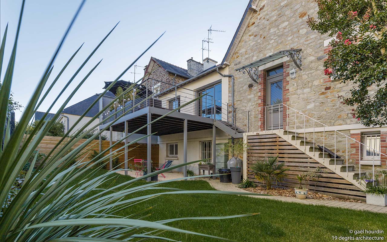 Extérieur de la maison côté jardin. Une terrasse sur pilotis a été créée, ce qui permet d'obtenir un coin détente en dessous de celle-ci avec des fauteuils de jardin.