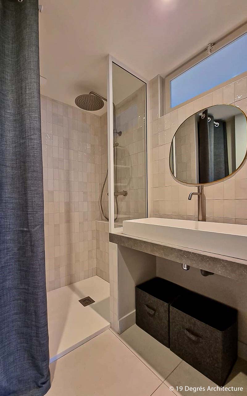 Salle de bain avec une douche et un vasque simple. l'ensemble des murs sont carrelés avec des petits carreaux gris.
