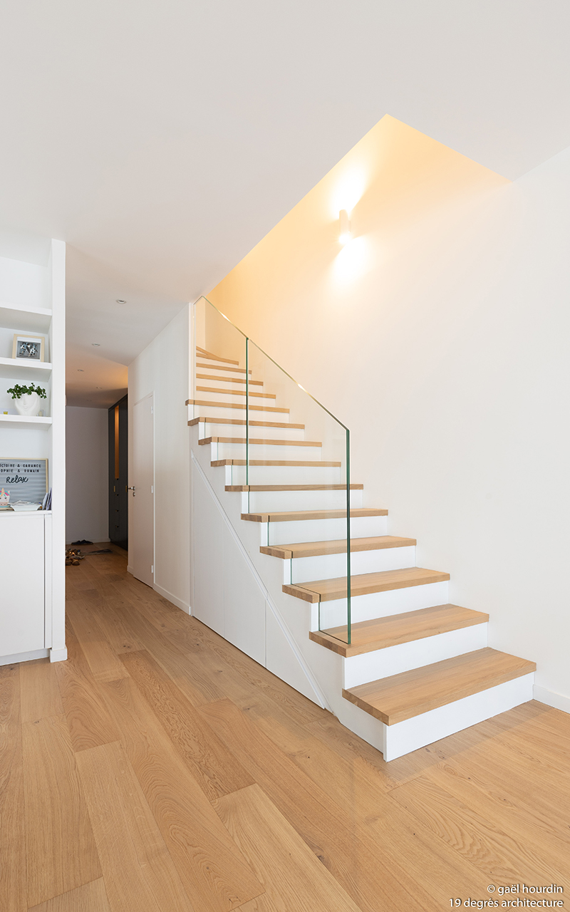 Escalier de couleur bois et blanc avec une vitre faisant office de barrière.