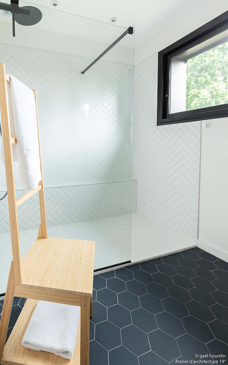 Salle d'eau avec une douche carrelée blanche. Le sol est en carrelage hexagonal noir afin de contraster la pièce.