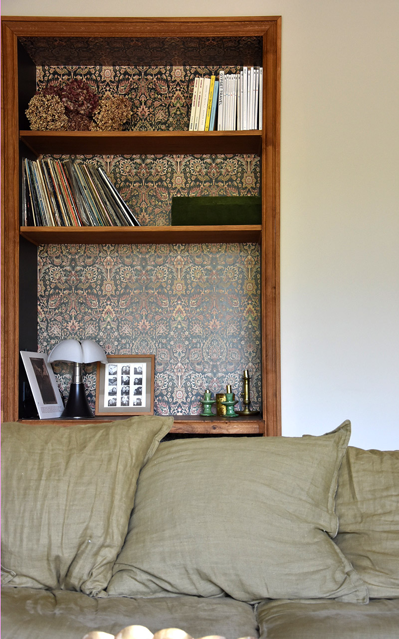 Bibliothèque intégrée au mur derrière un canapé vert en tissus.