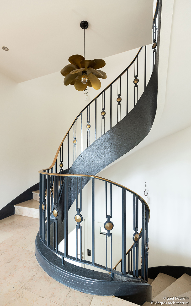 Escalier avec marches en marbre. La barrière est composée de différents métaux. Une suspension illumine l'escalier.