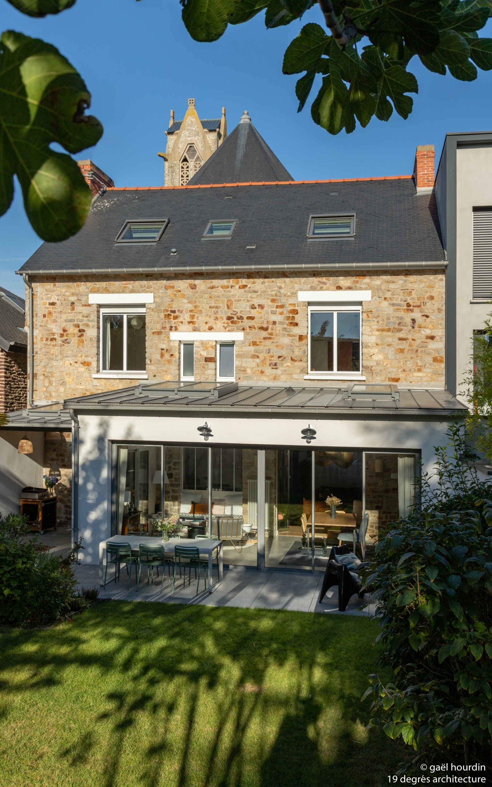 Extérieur de la maison avec la maison initiale en pierre et l'extension en enduit blanc. La maison possède une jardin arboré.