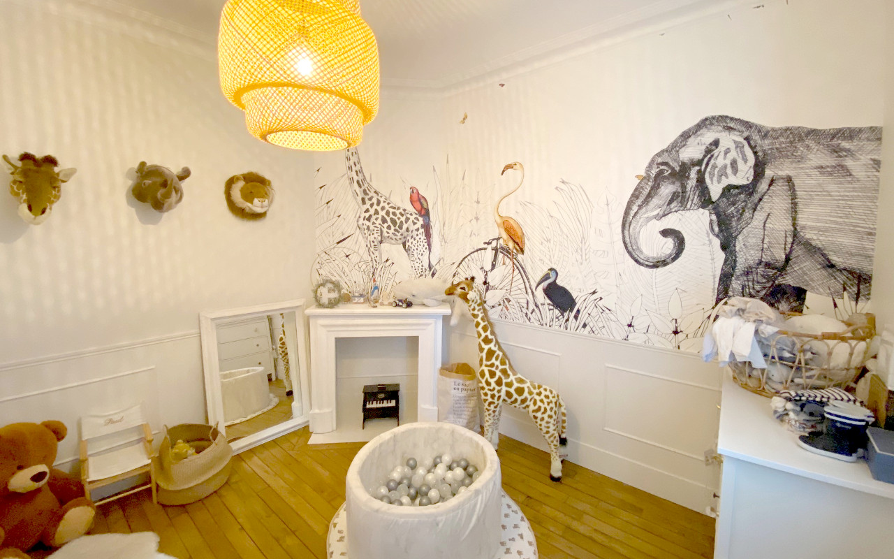 Chambre d'enfant sur le thème des animaux de la jungle. Fresque au mur d'un éléphant et d'une girafe ainsi que divers éléments de décoration sur ce thème.