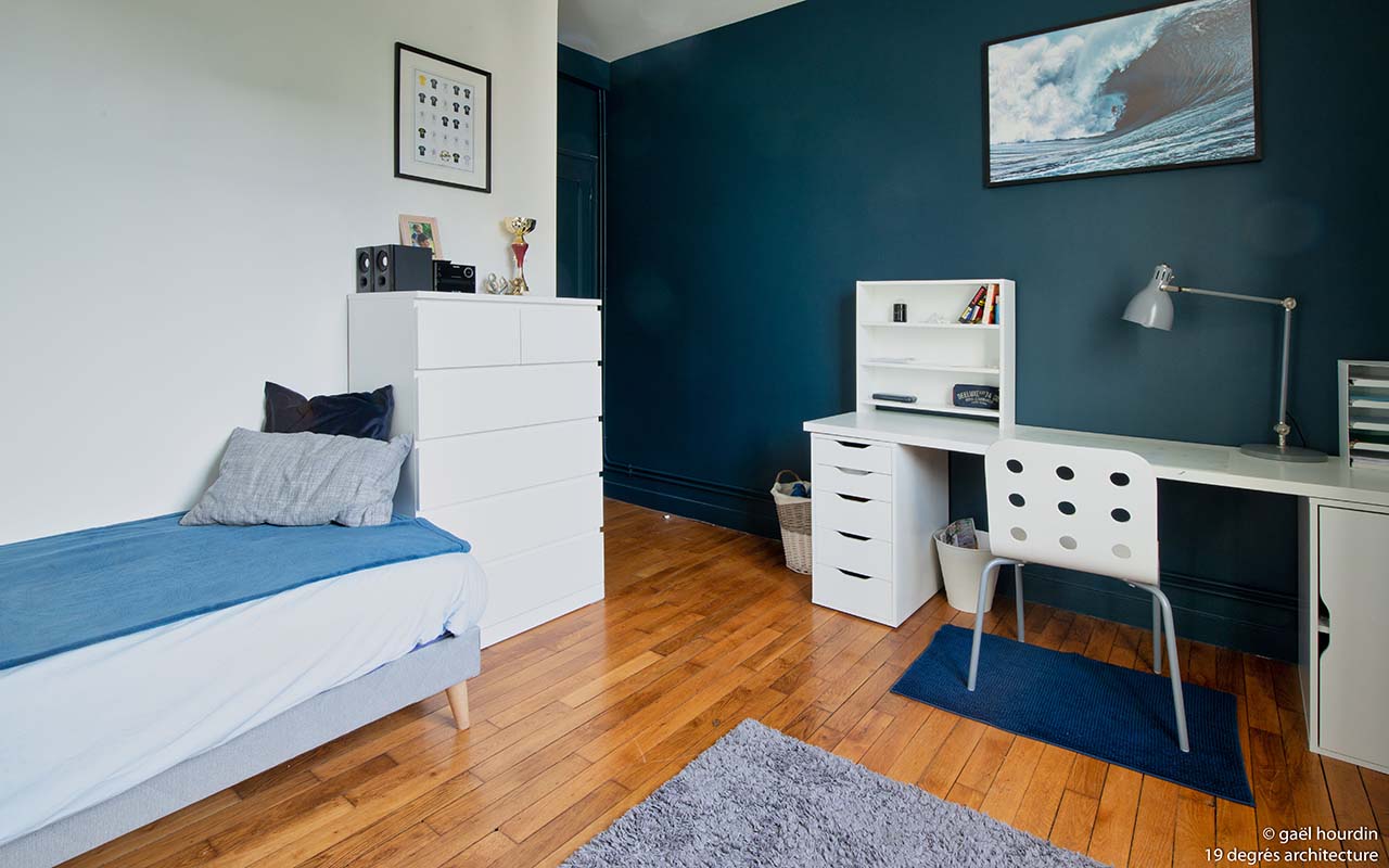 Chambre de garçon avec un lit simple, une peinture aux murs bleue et un bureau blanc.