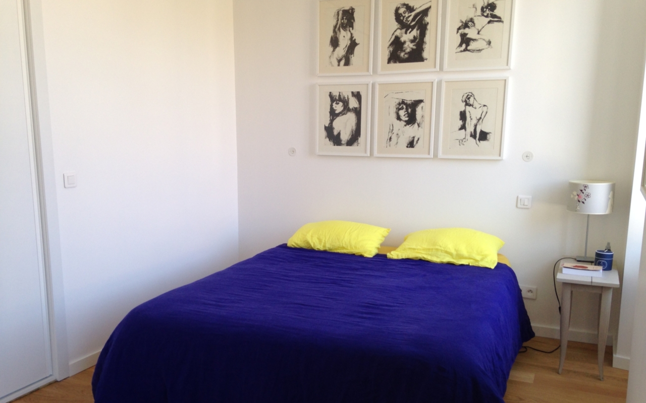 Chambre avec des tableaux en tête de lit. Les draps sont bleu foncé et jaune.