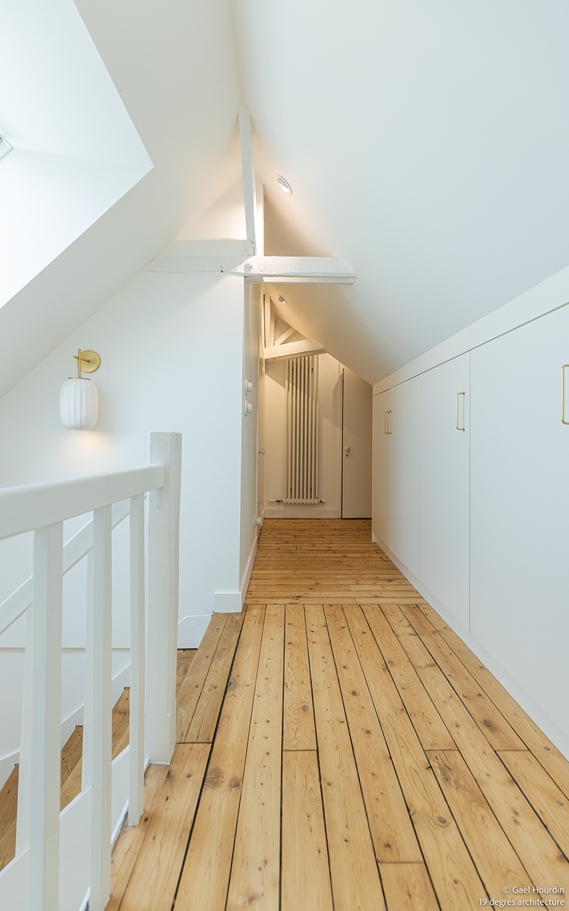Couloir blanc avec un sol en bois et escaliers.