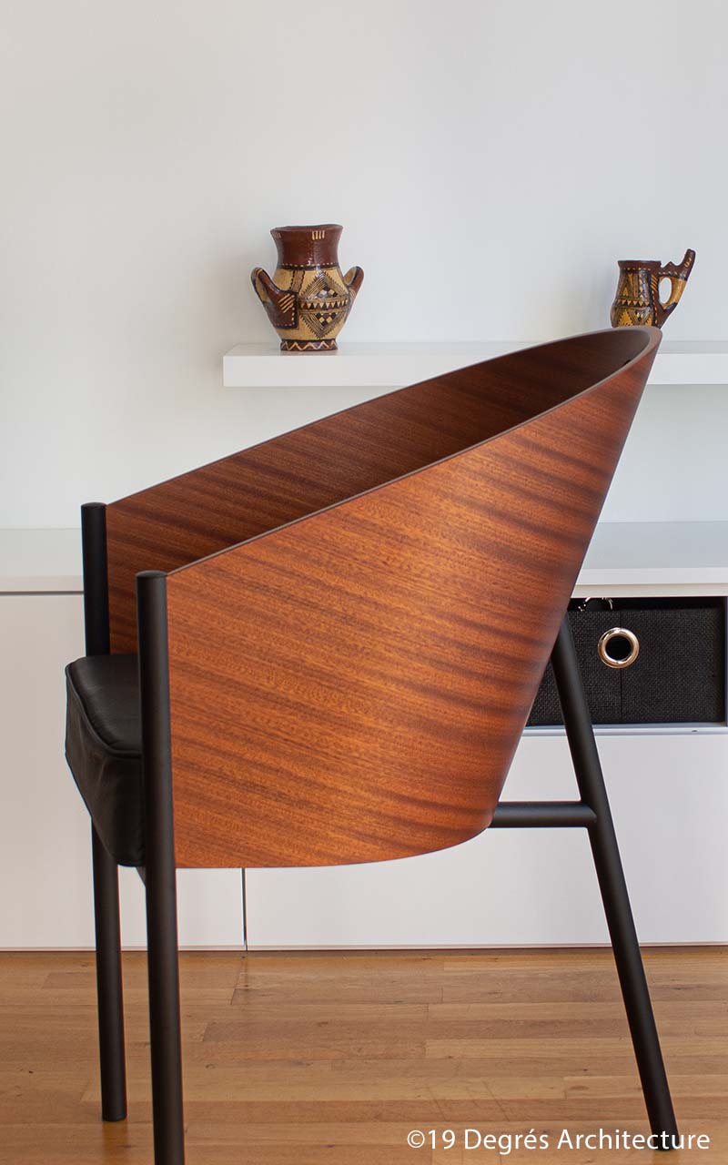 Photo du fauteuil en bois présent dans le salon. Il comporte un dossier en matière bois et une assise en cuir.